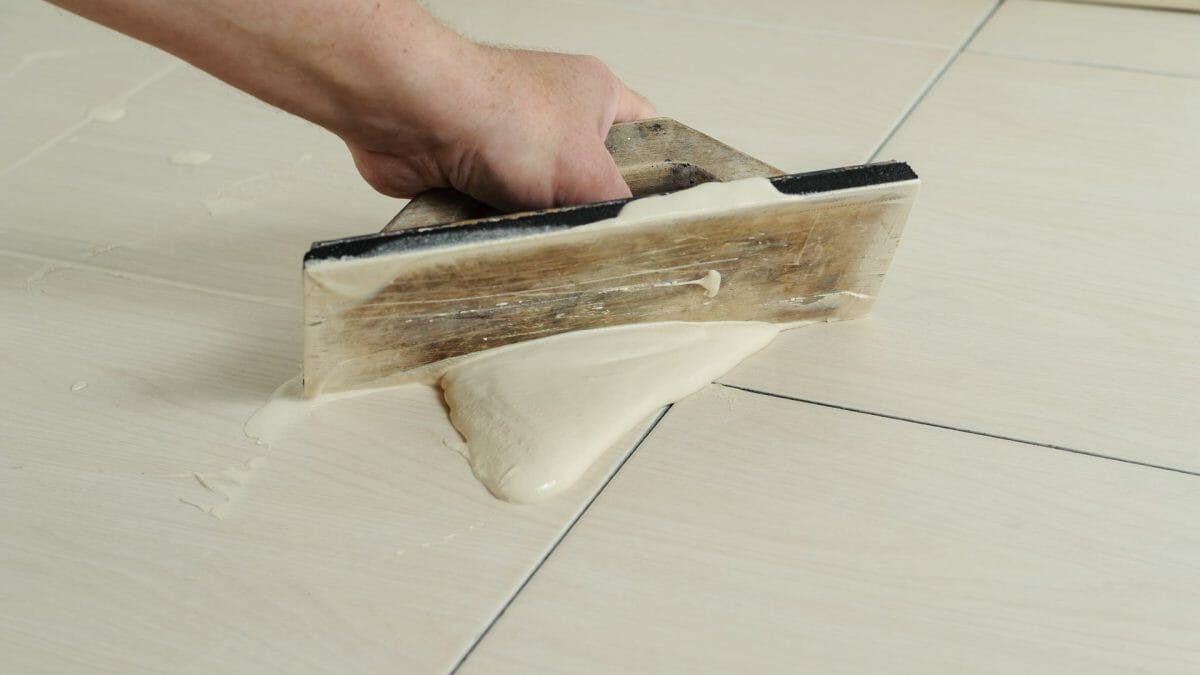 The hand of man holding a rubber float and filling joints with grout